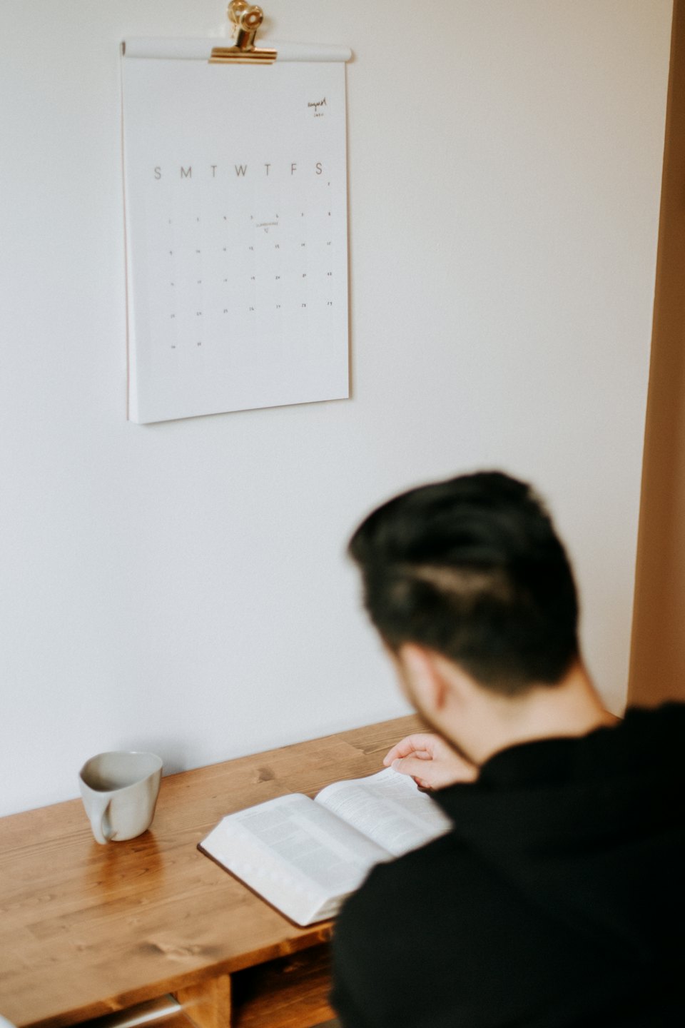 Persona leyendo un libro en un escritorio con una taza.