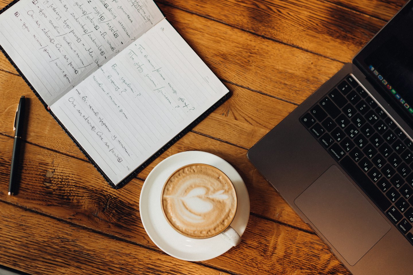 Portátil, cuaderno y café sobre un escritorio de madera.